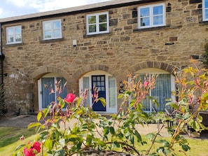 Traditional stone building with a central entrance and symmetrical facade, surrounded by a beautiful garden.