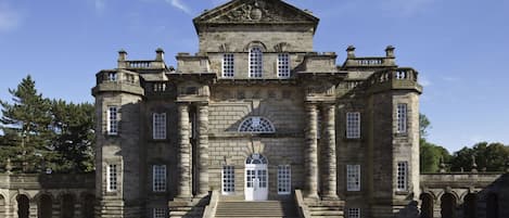 A large, historic stone building with a central entrance, flanked by symmetrical wings and a prominent central tower.