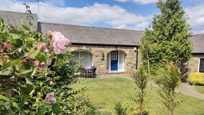 A stone cottage with a blue door, a lawn, and a garden with pink flowers. - Honeysuckle Cottage - one‑bedroom, dog‑friendly cottage with countryside feel (Cramlington)