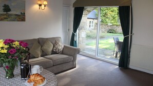 A cozy living room with a sofa, a coffee table, and a view of the garden through a sliding glass door. - Honeysuckle Cottage - one‑bedroom, dog‑friendly cottage with countryside feel (Cramlington)
