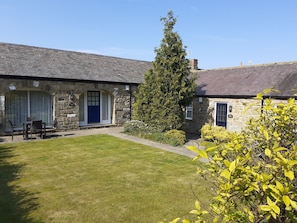 A stone building with a blue door, a lawn, and a tall tree.