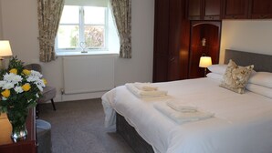 A hotel room with a large bed, two bedside lamps, a window with curtains, a radiator, a wooden wardrobe, and a vase with flowers. - Honeysuckle Cottage - one‑bedroom, dog‑friendly cottage with countryside feel (Cramlington)