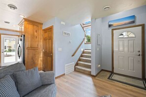 A hallway with a wooden door, a staircase, a couch, and a sign on the wall. - Retreat at Sunshine Creek, Downtown Fish Creek (Fish Creek)