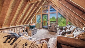 Une chambre mansardée chaleureuse, avec un plafond en pente, une grande fenêtre et une vue sur l’extérieur.
