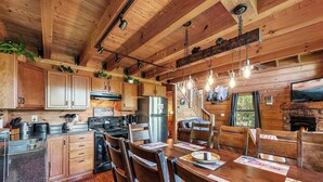 L’intérieur d’un chalet rustique, avec des murs en bois, une cuisine équipée d’appareils modernes, un coin repas avec des tables et des chaises en bois, et une cheminée.
