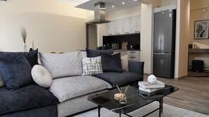 A modern living room with a grey sofa, black coffee table, and a kitchen area in the background.