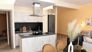 A modern kitchen with a central island, a dining area with a glass table, and a living room with a sofa and decorative plants.