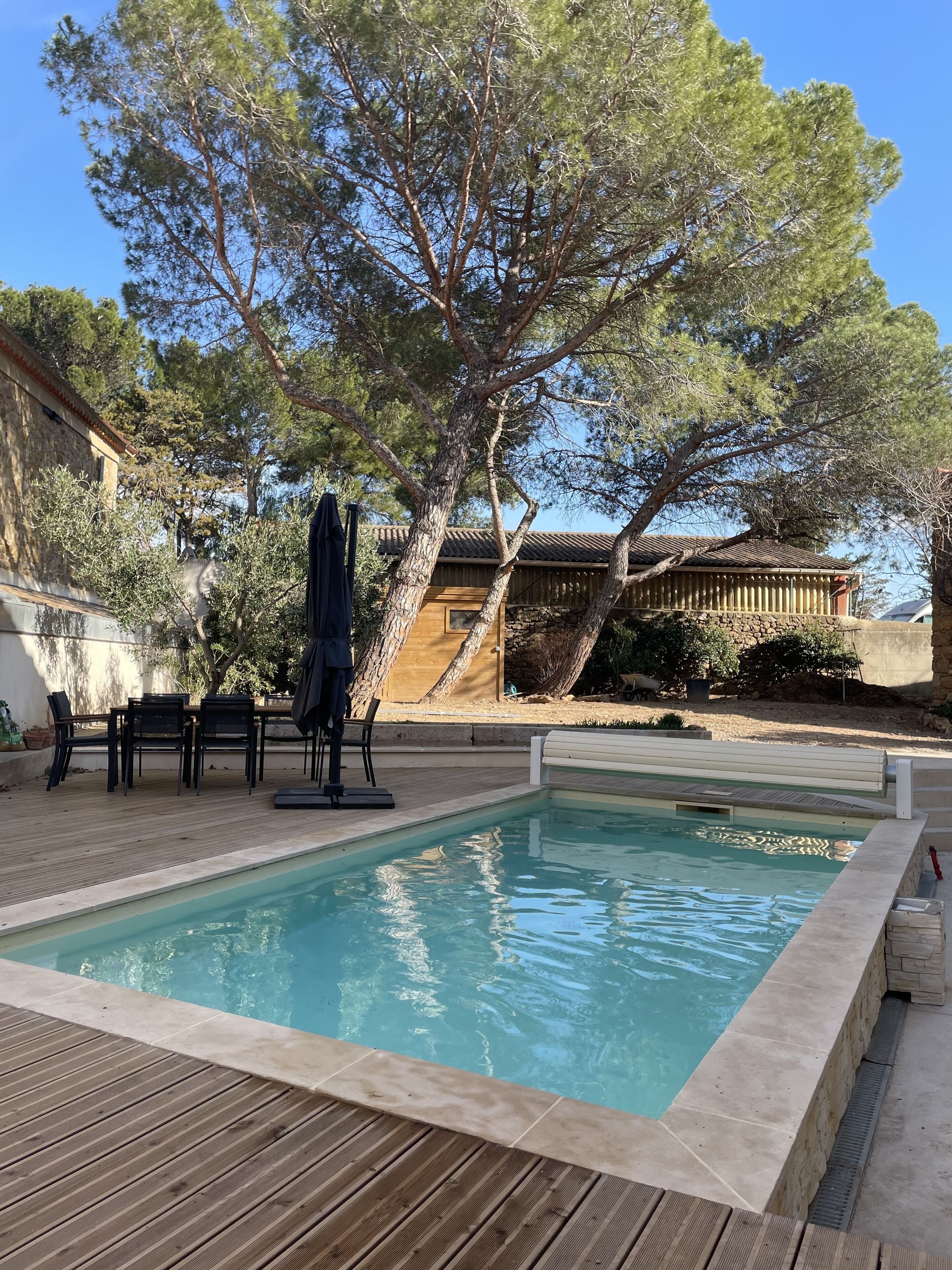 Una piscina con cubierta de madera, rodeada de árboles y un edificio con techo de tejas.
