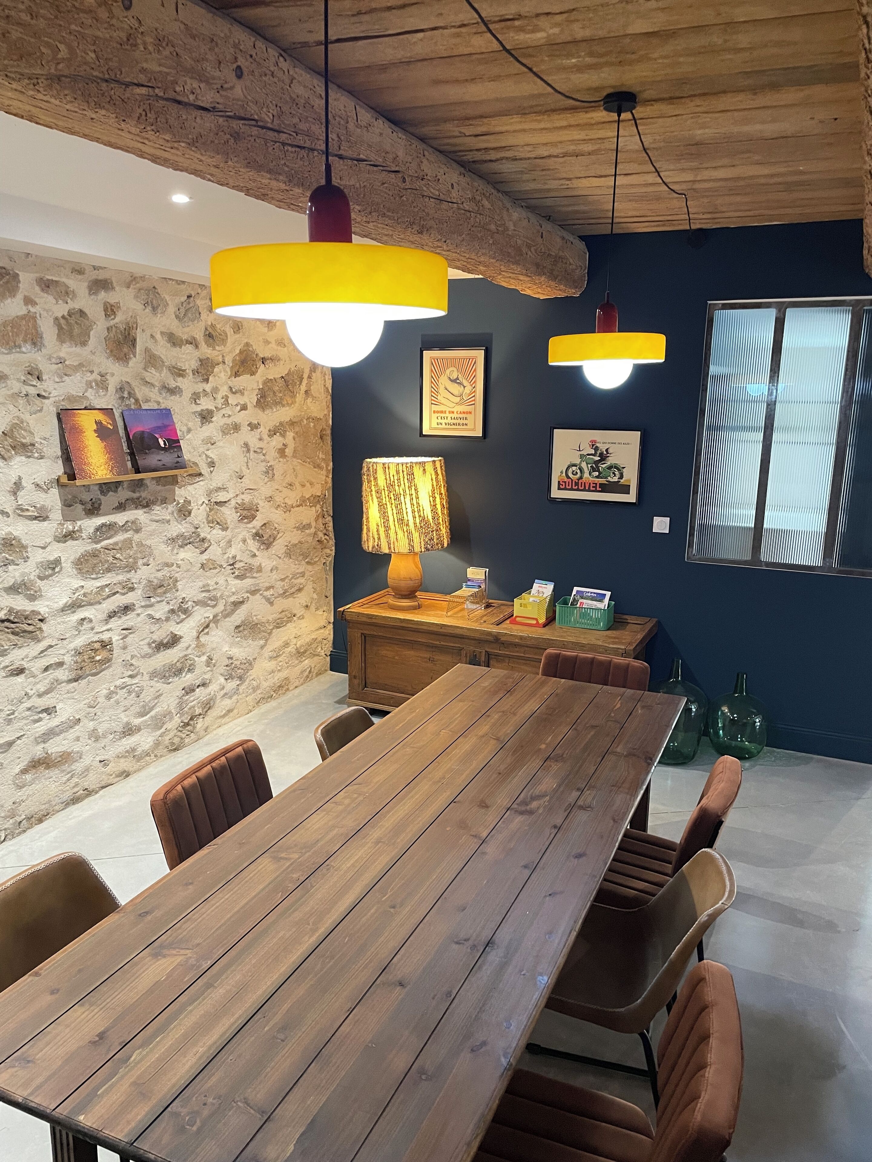 A dining area with a wooden table, chairs, a lamp, and a stone wall.