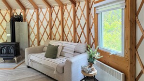 A cozy room with a wooden ceiling, a sofa, a small table with a plant, a window, and a fireplace.