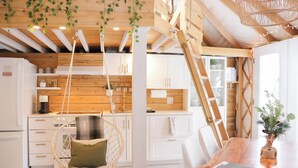 A modern kitchen with wooden beams, white cabinets, a hanging chair, and a dining table with a plant.
