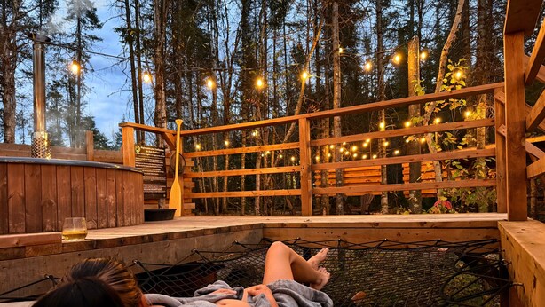 A wooden deck with a hammock, surrounded by trees and string lights.