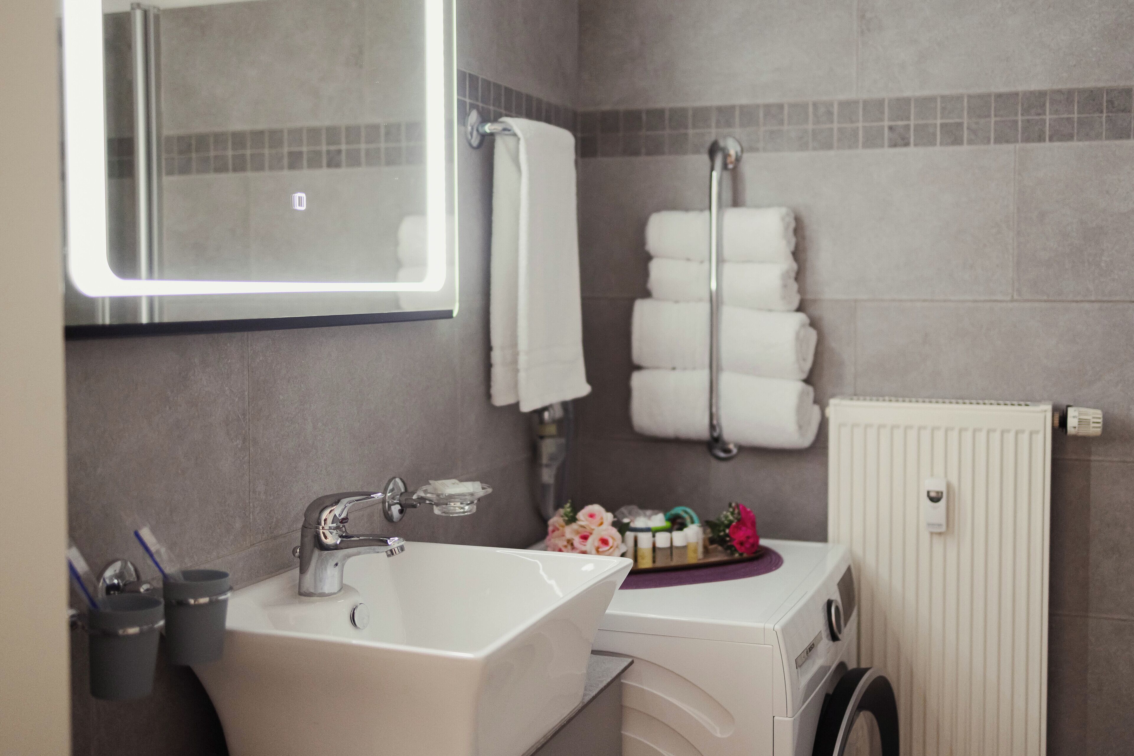 A bathroom with a sink, mirror, towel rack, and a washing machine.