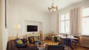 Een woonkamer met een bank, stoelen, een salontafel, een televisie en een eethoek met een tafel en stoelen.