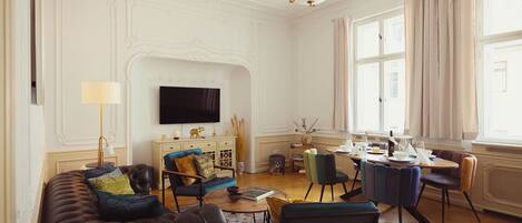 A living room with a sofa, chairs, a coffee table, a TV, and a dining area with a table and chairs.