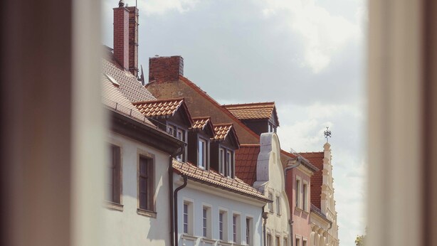 Een geplaveid straatje omzoomd door historische gebouwen, een heldere lucht, en enkele voetgangers.