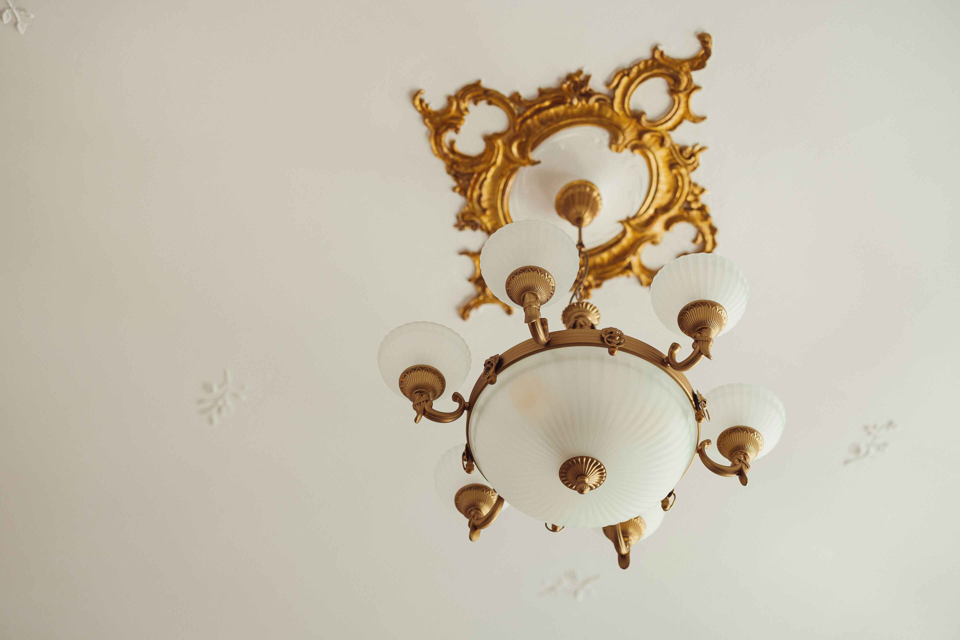 Un lampadario con più bracci e paralumi in vetro, fissato a una parete con una cornice dorata decorativa.
