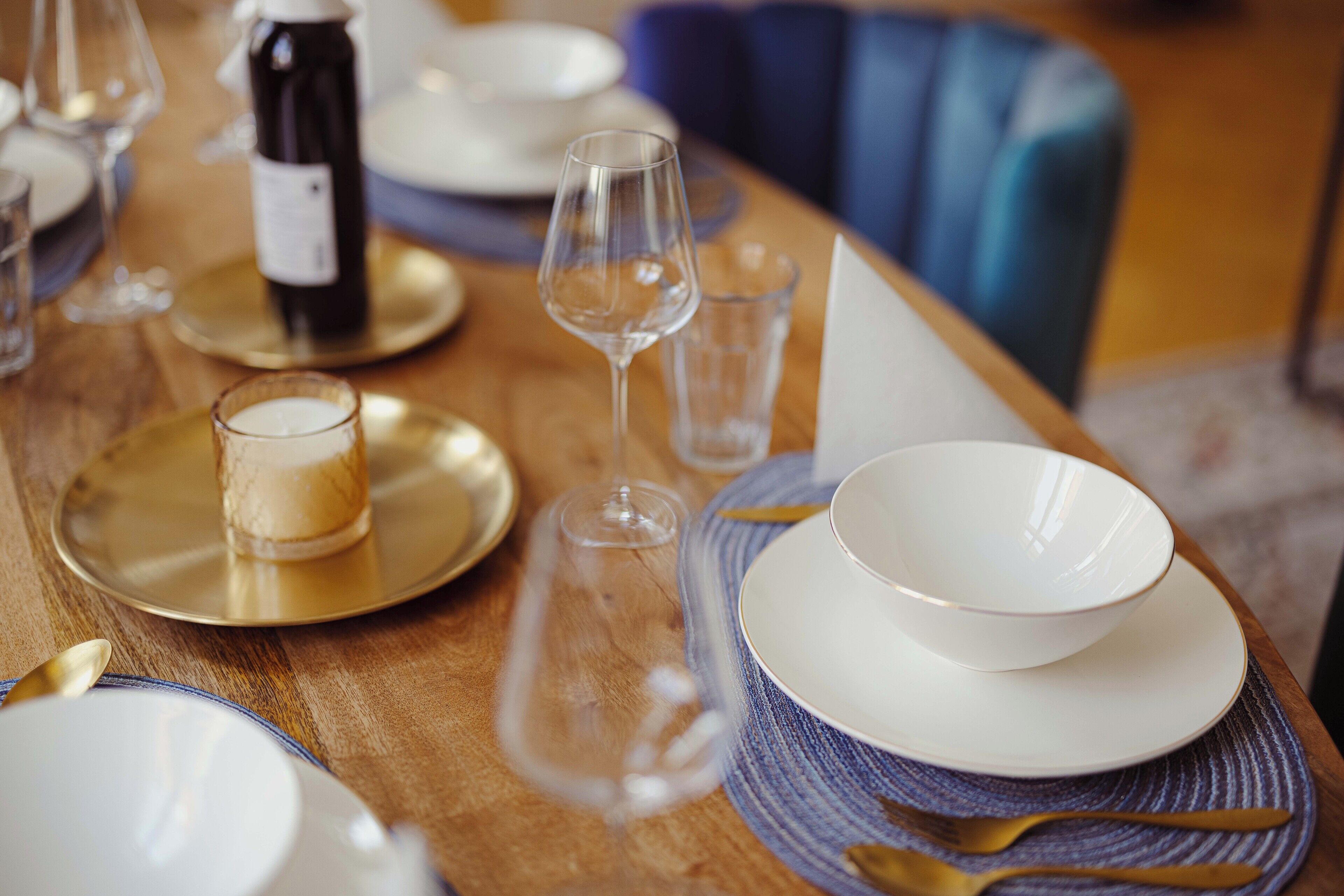A dining table set with plates, glasses, and a bottle of wine.