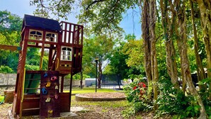 A wooden play structure with climbing holds and a slide, surrounded by trees and a grassy area.