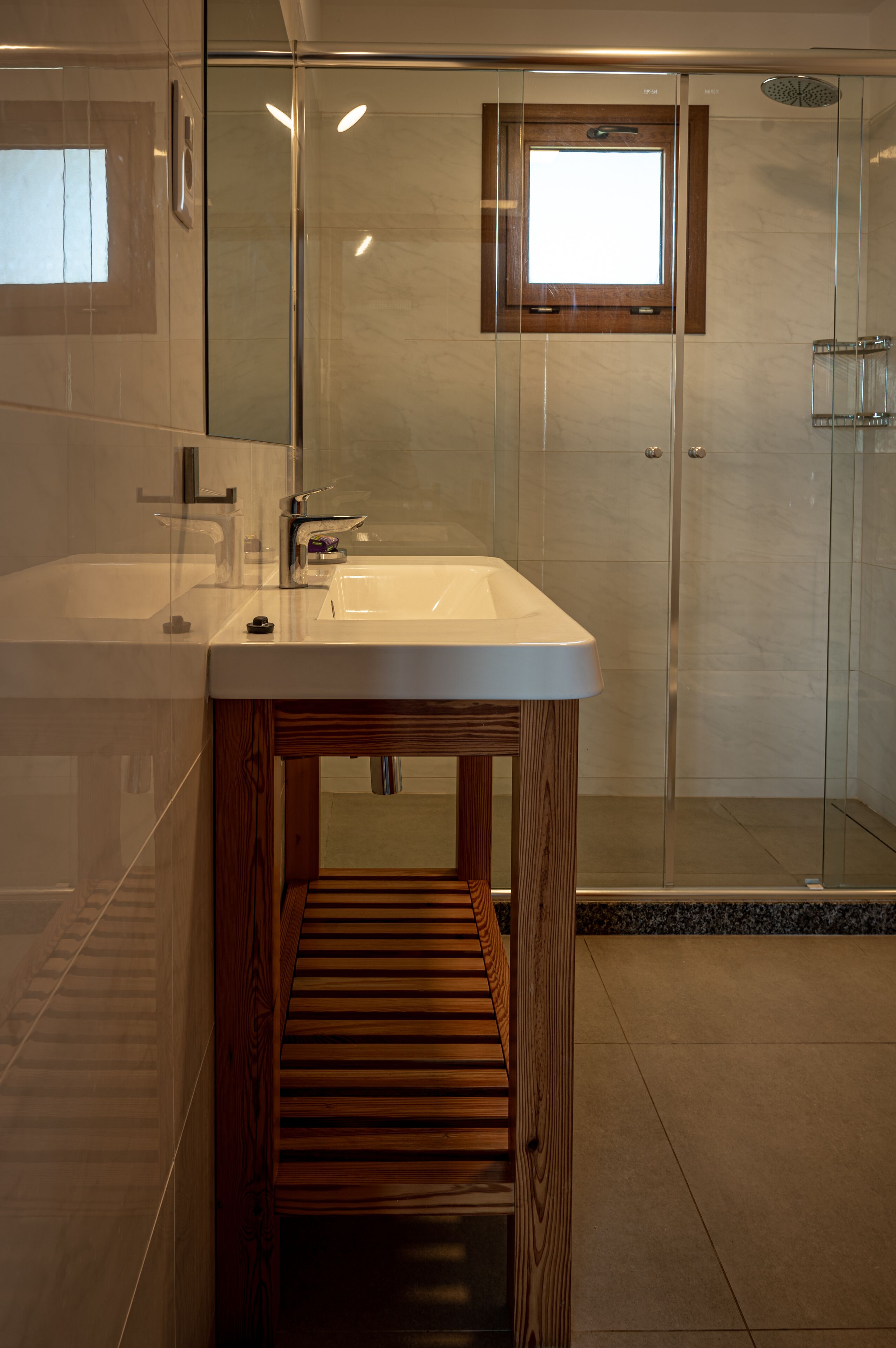 A modern bathroom with a glass-enclosed shower, a wooden vanity, and a large mirror.