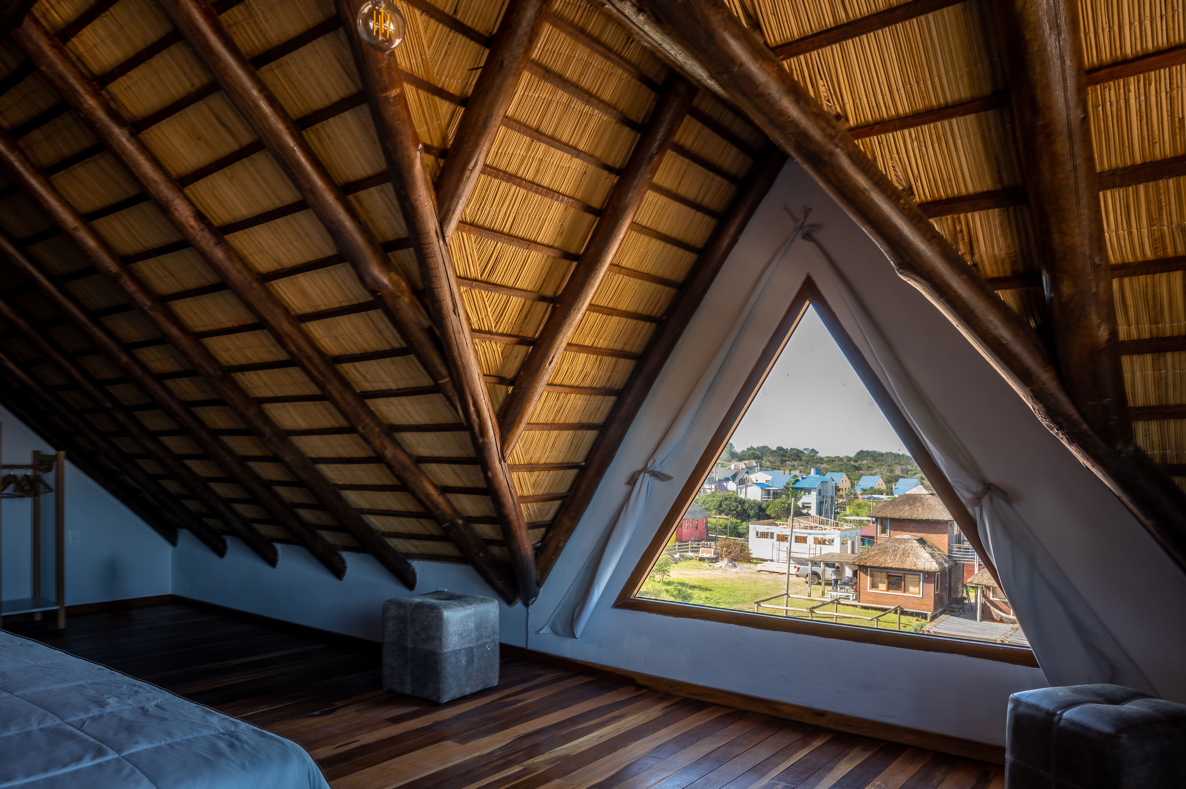 A room with a sloped ceiling, wooden beams, and a large window offering a view of buildings outside.