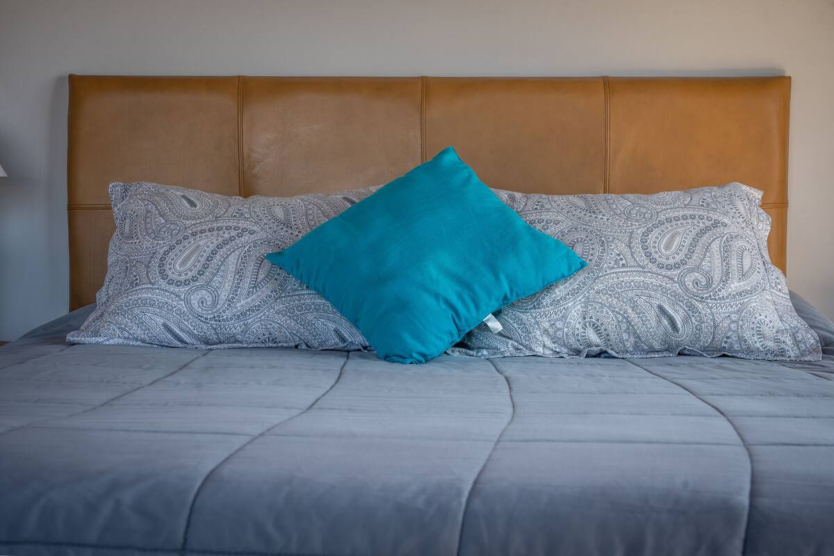 A bed with a grey quilt and two patterned pillows, one teal and one grey.