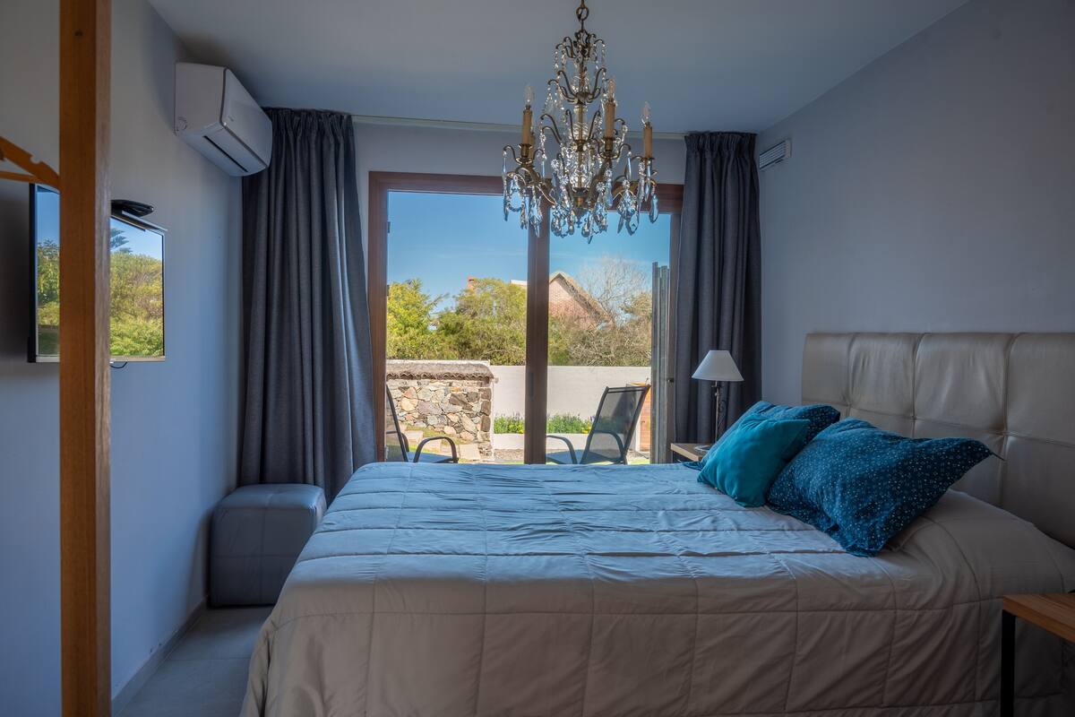 A bedroom with a large bed, a chandelier, a TV, and a view of the outdoors.