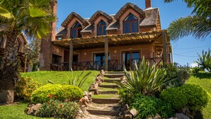 A large, two-story house with a brick exterior, a wooden porch, and a stone staircase leading to the front door. - Muelles del Diablo Tranquilo (Punta del Diablo)