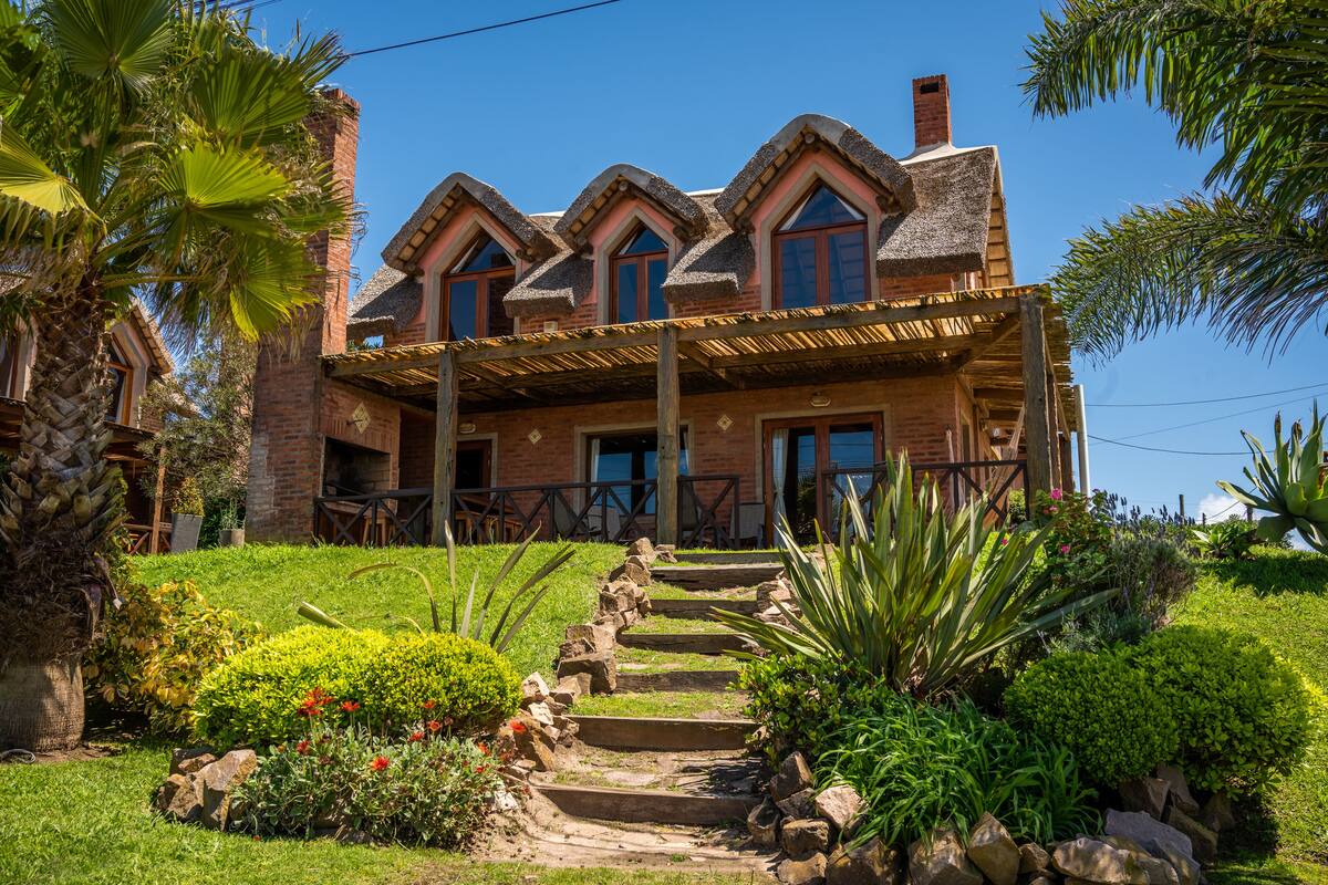A large, two-story house with a brick exterior, a wooden porch, and a stone staircase leading to the front door.