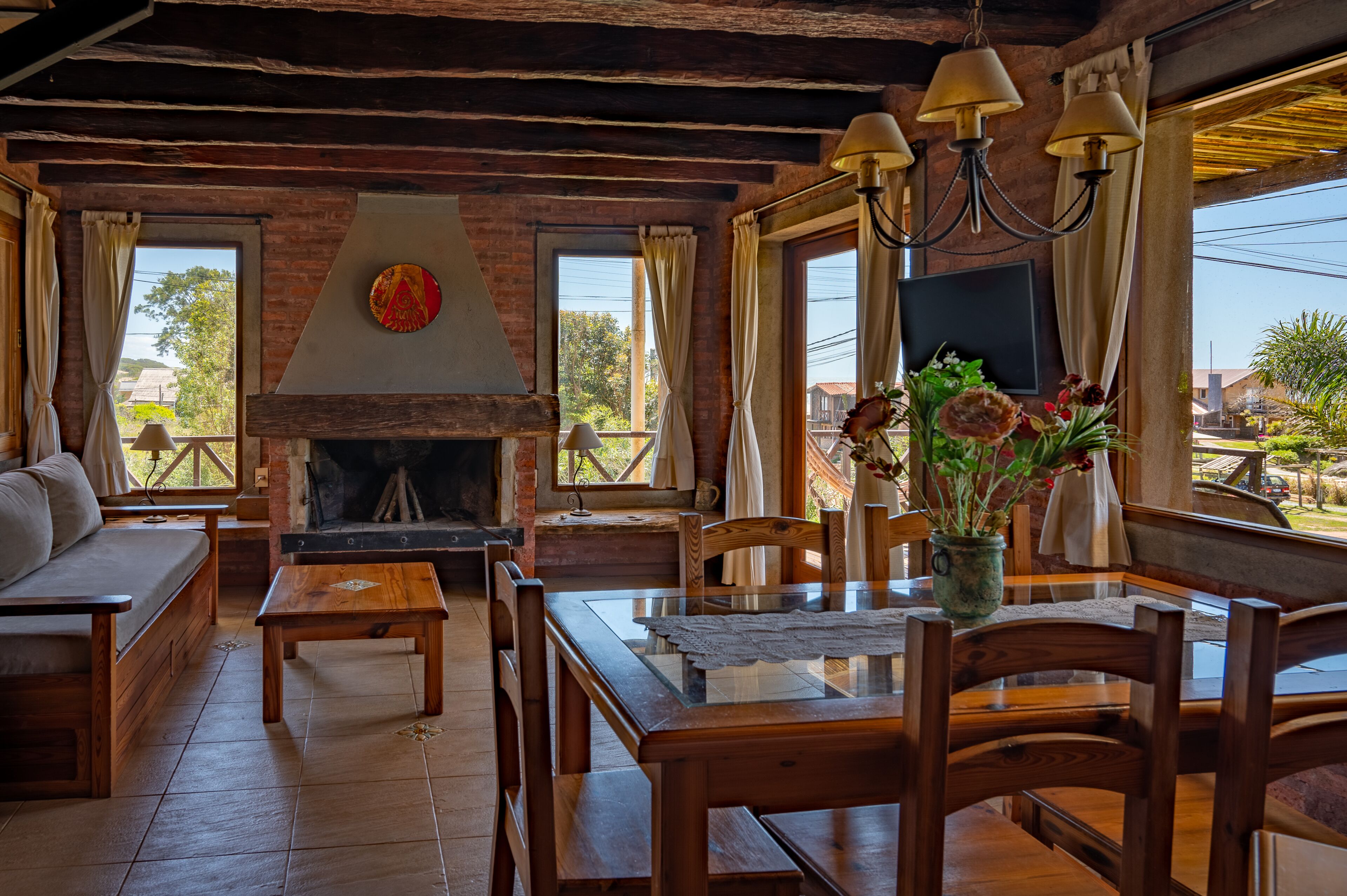 A cozy room with a fireplace, wooden furniture, and large windows offering a view of the outdoors.