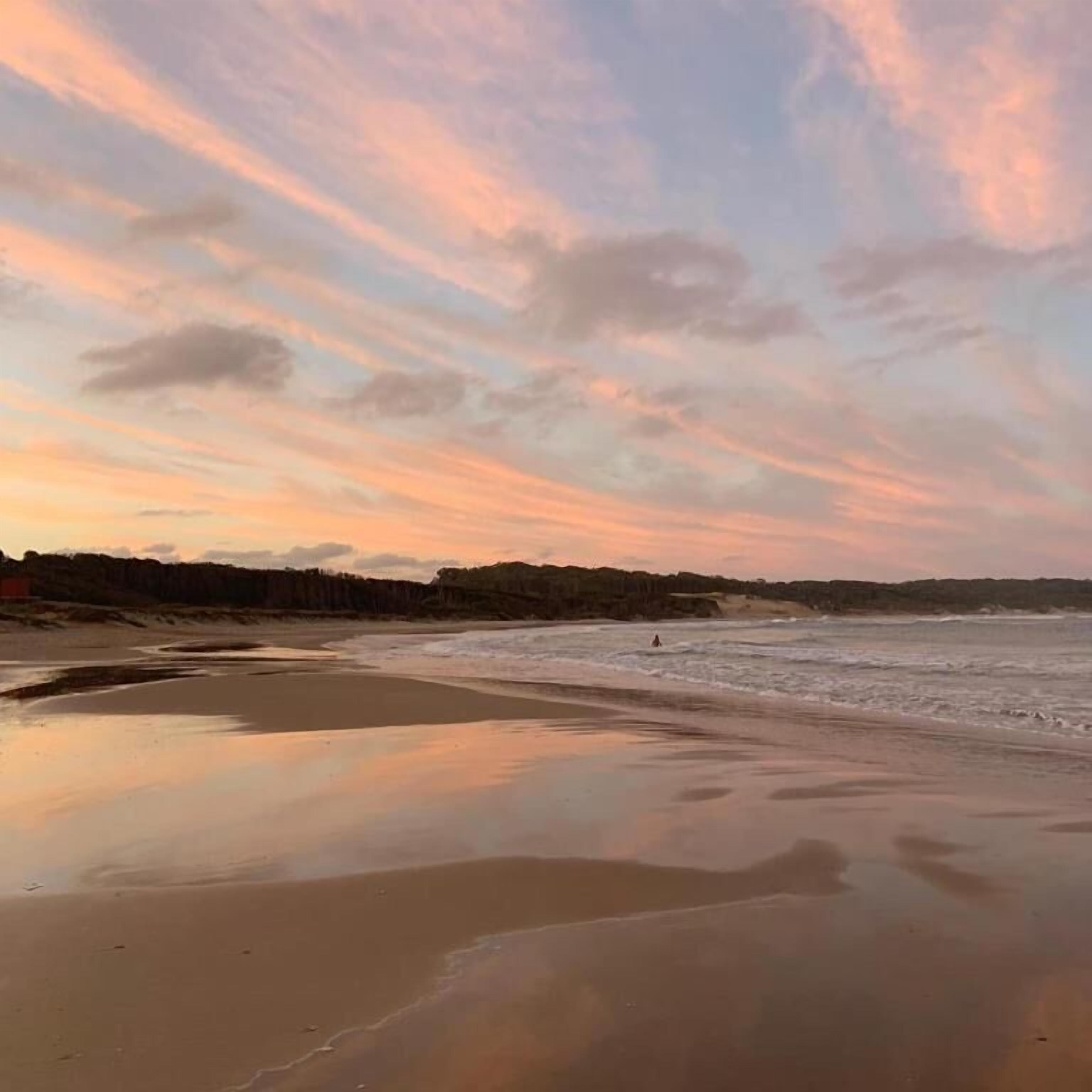 Una spiaggia con mare calmo, la sabbia bagnata in primo piano e un cielo al tramonto.