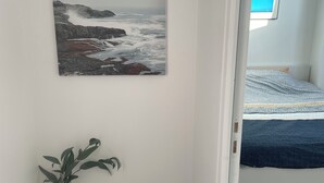 Ein Zimmer mit einem Bett, einem gerahmten Bild einer felsigen Küste und einer Vase mit weißen Blumen.