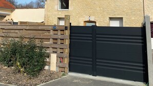 Ein zweistöckiges Haus mit einem Ziegeldach, einer schwarzen Garagentür und einem Holzzaun.