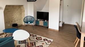 Ein modernes Wohnzimmer mit einer Steinwand, einem blauen Sessel, einem weißen Tisch, einem Fernseher auf einer Holzkommode und einer Treppe.