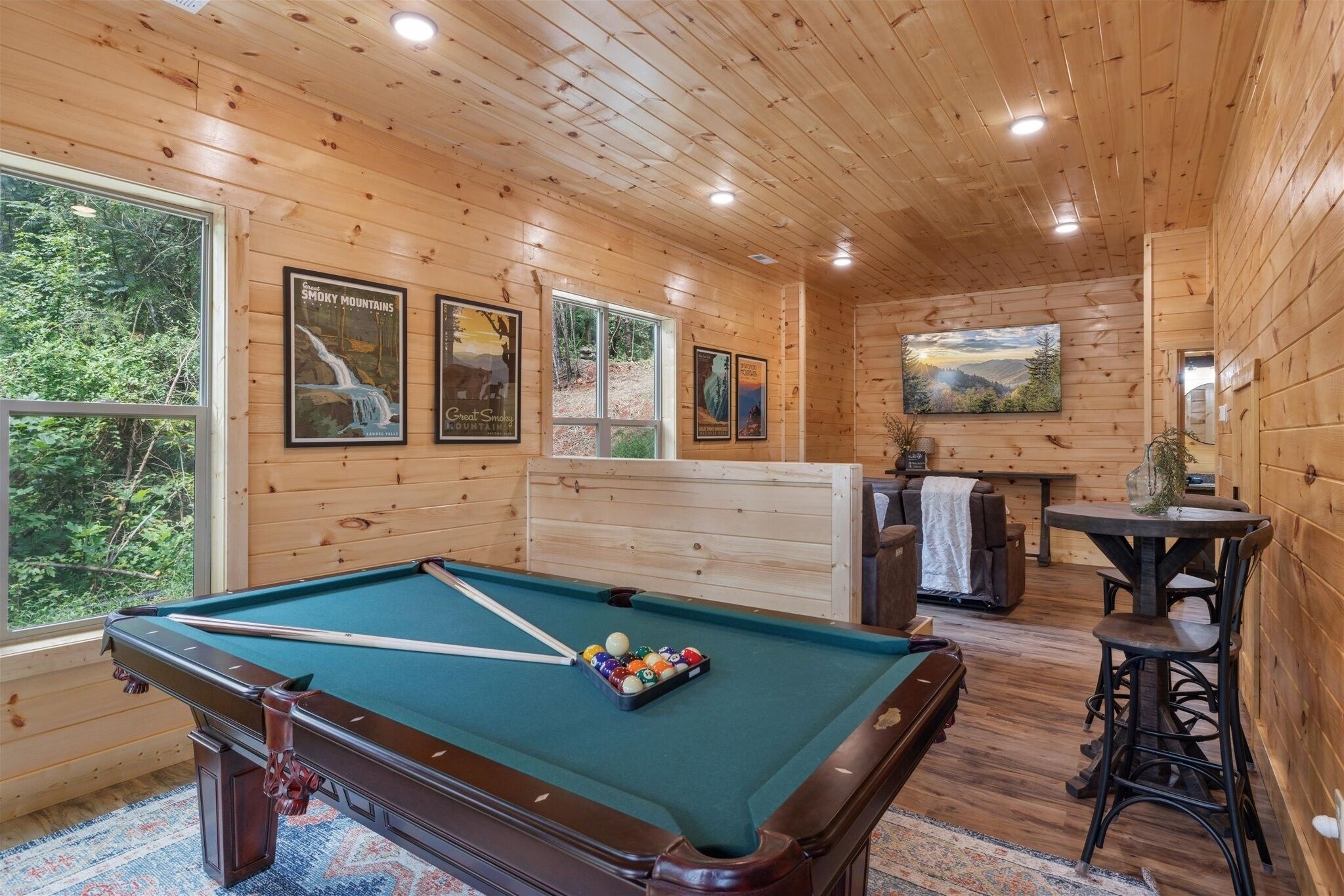 A pool table with balls, wooden walls, and framed pictures of mountains.