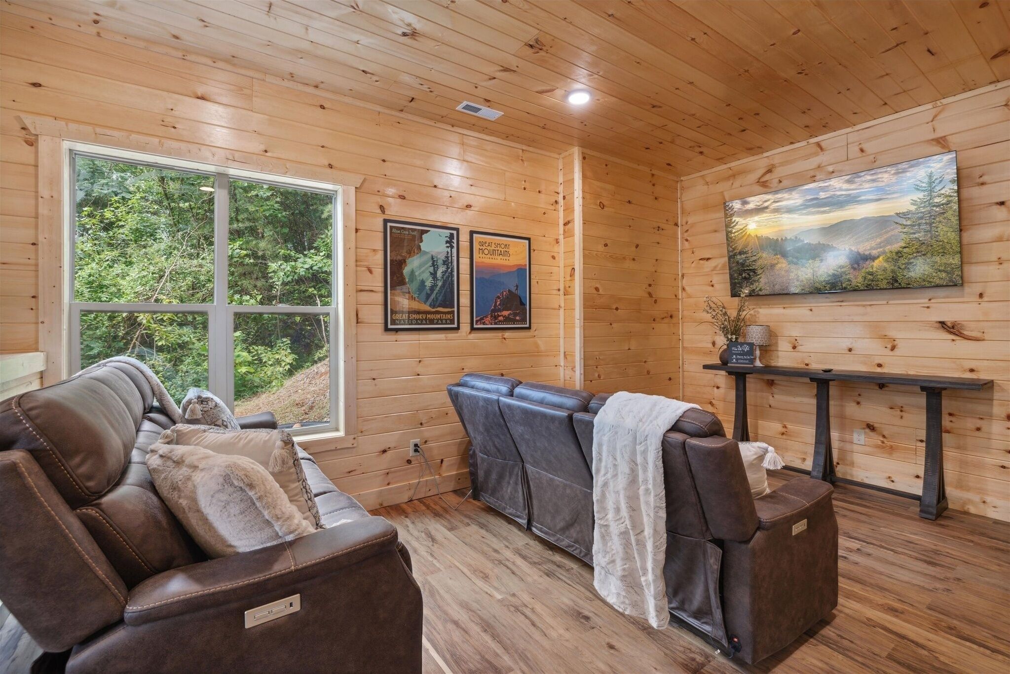 En stuga med träpanel på insidan, utrustad med en soffa som kan fällas tillbaka, en massagestol och ett stort fönster med utsikt över skogen.