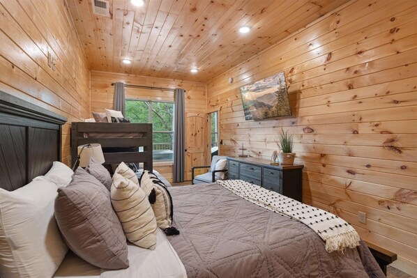A wooden-paneled bedroom with a bed, dresser, and a painting on the wall.