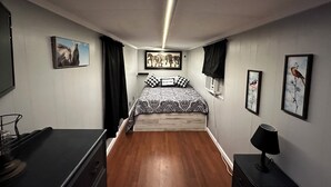 Ein Schlafzimmer mit Holzboden, einem Bett mit gemusterten Textilien, einem Schreibtisch mit Lampe und gerahmten Bildern an den Wänden.