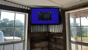 Ein Zimmer mit an der Wand montiertem Fernseher, der ein Einstellungsmenü anzeigt, Holzwänden und großen Fenstern.