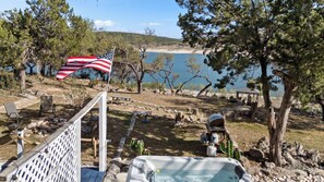 Un terrain de camping équipé d’un mât pour drapeau, d’une table de pique-nique, de chaises, d’un bain à remous et offrant une vue sur un lac.