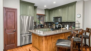 A kitchen with green cabinets, stainless steel appliances, a granite countertop, and a wooden island with bar stools.