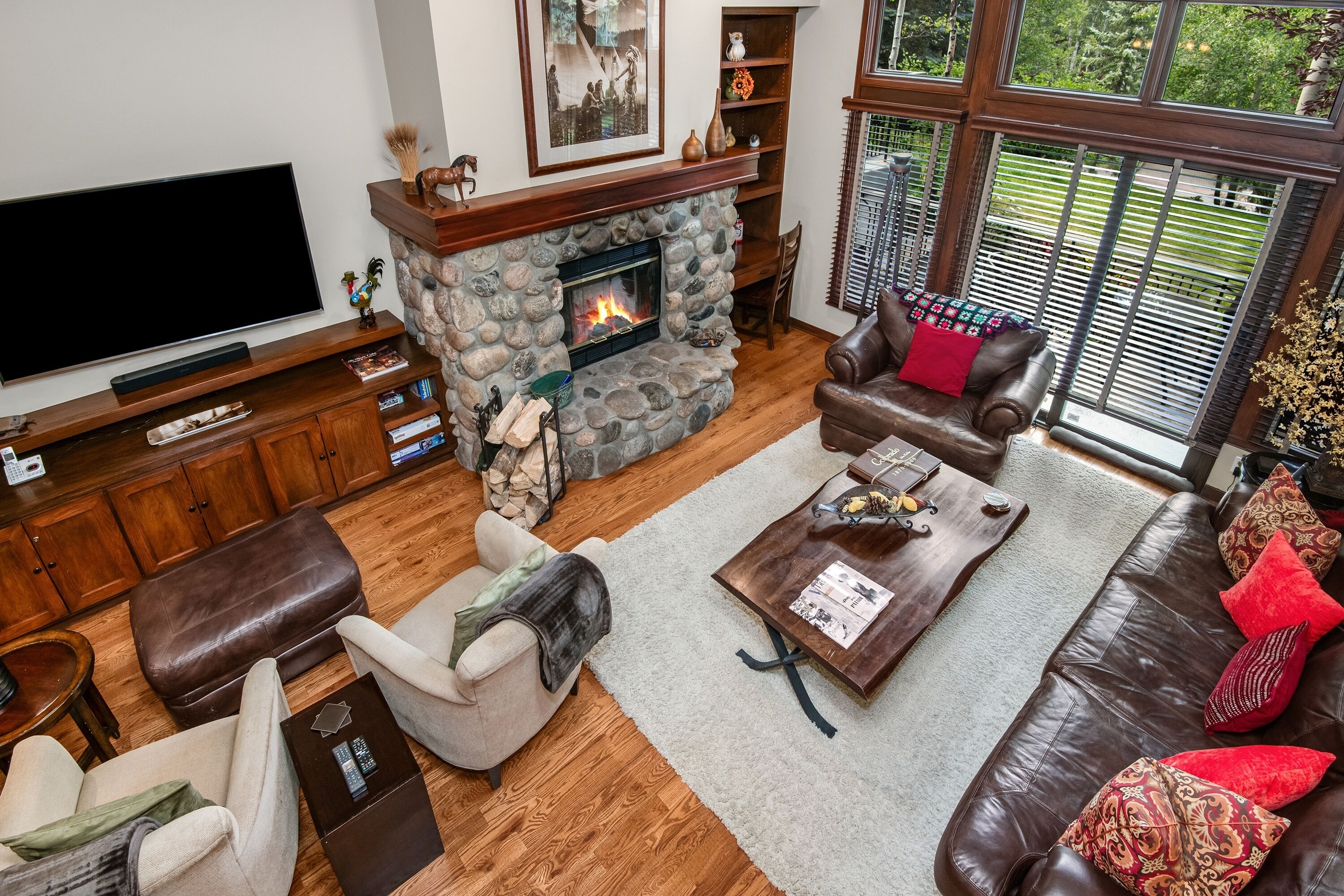 A living room with a stone fireplace, leather furniture, a flat-screen TV, and a bookshelf.