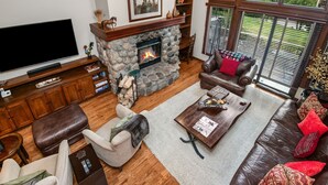 A living room with a stone fireplace, leather furniture, a flat-screen TV, and a bookshelf.