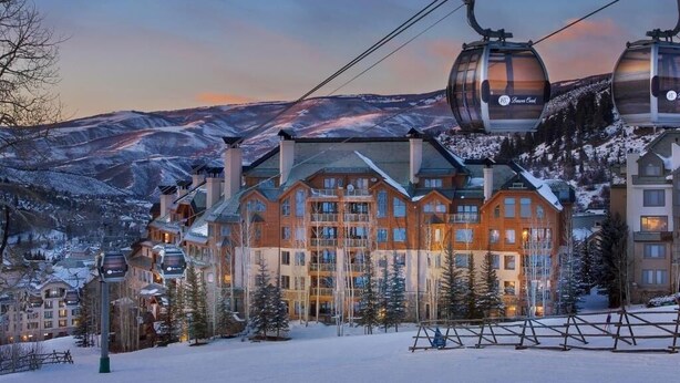 A ski resort with a cable car system, a large lodge building, and snow-covered mountains in the background.