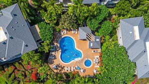 An aerial view of a resort with a central swimming pool surrounded by lounge areas and palm trees. - Grand Champions 30 2 Bedroom Condo (Kihei)