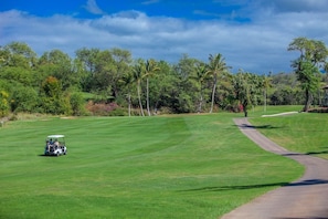 A golf course with a golf cart, trees, and a clear sky.