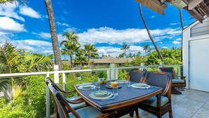 An outdoor dining area with a table set for four, surrounded by wicker chairs with cushions.