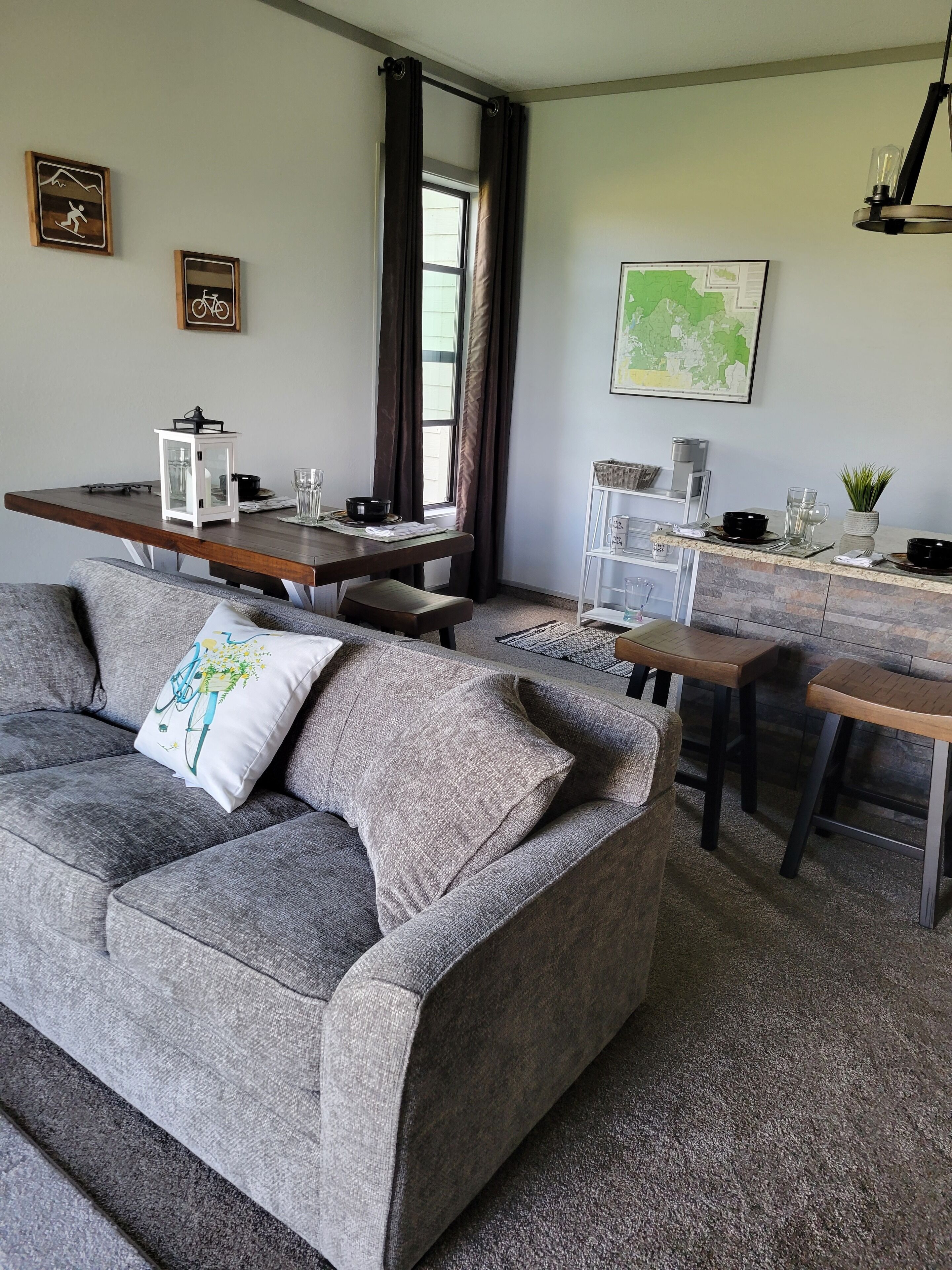 Un salon moderne avec un canapé gris, une table à manger en bois et un coin cuisine agrémenté d’une carte au mur.