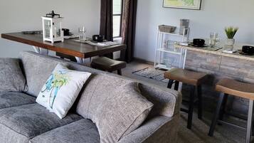 Un salon moderne avec un canapé gris, une table à manger en bois et un coin cuisine agrémenté d’une carte au mur.