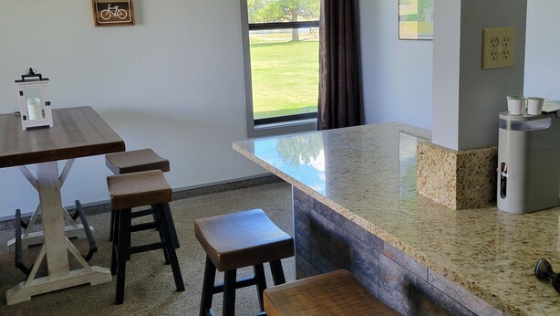 Una cocina moderna con encimera de granito, taburetes de madera, una lámpara colgante y vistas al exterior a través de una ventana.